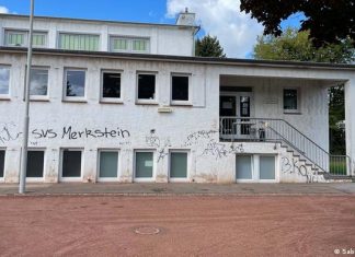Refugees: German cities are reaching their limits | Germany | DW Gymnasium in Herzogenrath-Merkstein with stairs and entrance on the right. In the front there are two rows of windows, one above the other. The facade is white but shows clear traces of dirt and the red sand of the sports field in front and scribbles in black paint.