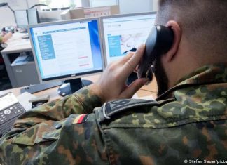 Ukraine war: Bundeswehr prepares for homeland security Germany | DW A uniformed Bundeswehr soldier makes a phone call while sitting at a desk with two computer screens.