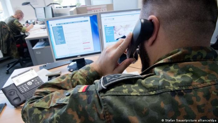Ukraine war: Bundeswehr prepares for homeland security Germany | DW A uniformed Bundeswehr soldier makes a phone call while sitting at a desk with two computer screens.