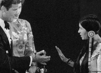 Sacheen Littlefeather is dead | culture | DW Sacheen Littlefeather makes a defensive hand gesture, Roger Moore looks at her with trophy in hand, Liv Ullman in the middle